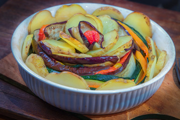 Baked spiral of red pepper, eggplant, onion,tomatoes, young potatoes and zucchini in white ceramic shape.