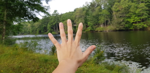 left Human hand with extended fingers to hight five in nature next to a river