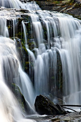 Fototapeta na wymiar Mountain waterfall dropping over smooth moss rocks in blurred motion.