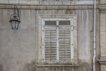 Fototapeta na wymiar Old window with peeling, painted, wooden shutters next to new street light