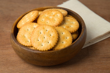 Round salted cracker cookies in wooden bowl putting on linen and wooden background.