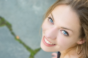 Portrait of a young woman blonde with blue eyes looking up, toothy smile.