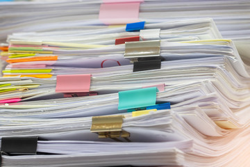 Close up pile of unfinished homework assignment stacked in archive with colorful paper clips on teacher's table waiting to be managed and inspected. Stack of paperwork. Education and business concept.