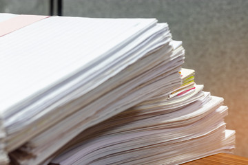 Close up pile of unfinished student's homework assignments on teacher's table in office waiting to be managed and inspected. Stack of paperwork and reports. Education and business concept.