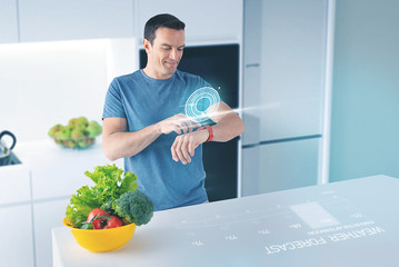 Happy man. Cheerful young man standing in a modern kitchen and smiling while looking at the...
