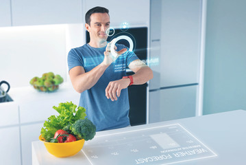 Bright projection. Positive confident nutritionist smiling and touching the hologram while using modern technologies in his work