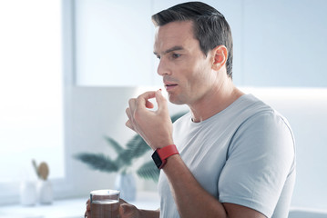 Taking pills. Handsome young man standing with a glass of water and taking pills while having an unbearable headache