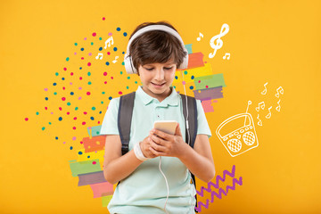 Great music. Positive happy boy looking at the smartphone in his hands while wearing big headphones and listening to music