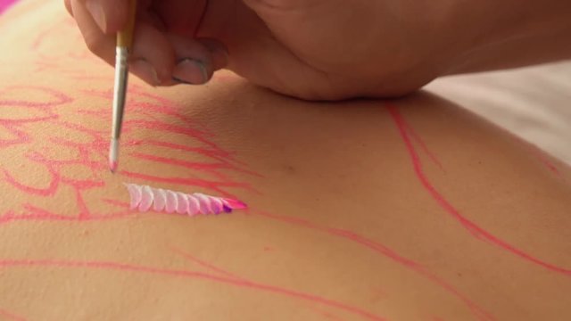 Master of Petrykivka decorative painting making smears on a human body. Focus on the hands of an artist.