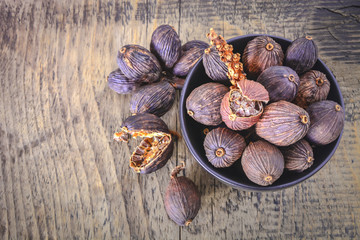 Black cardamom pods with open shell in ceramic bowl and Indian spice on wooden background.
