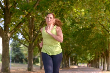 Gartenposter Fit middle-aged woman jogging through a park © michaelheim