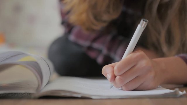 Slow-motion close-up detail of professional student pupil teen gilr writing in her notebook workbook