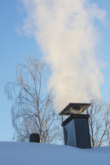 Smoke is coming from the chimney in Finland. In the background of the blue sky. It's winter and...