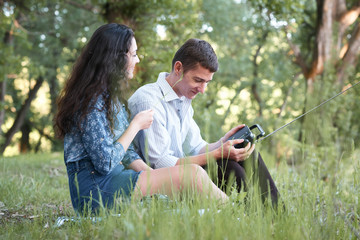 young couple sitting on the grass in the forest and looking on sunset, listen to radio, summer nature, bright sunlight, shadows and green leaves, romantic feelings