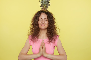 Pretty European woman practices yoga, feels relaxed and calm, shows mudra sign with both hands,...