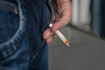 Guy holds a Smoking cigarette butt from the cigarette with two fingers.