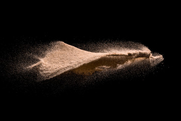 Dry river sand explosion. Golden colored sand splash agianst dark background.