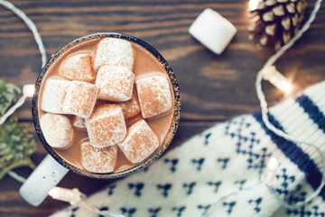 Hot cocoa with marshmallow in a white ceramic mug surrounded by winter things on a wooden table. The concept of cosy holidays and New Year. Top view, flat lay.