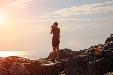 man traveler standing on a hill overlooking the sunset with camera travel concept