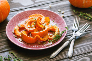 Baked pumpkin slices with thyme on a wooden board over grey table. Seasonal food vegetarian recipe.