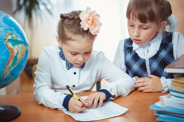 Two schoolgirls sit at a desk with a globe