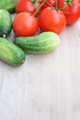 Freshly harvested cucumbers and tomatoes for preparing salad  on natural wooden board background with copy space for your text. Agricultural harvest and eco household vegetables concept.