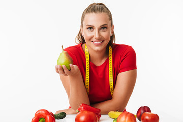 Pretty smiling girl with measuring tape on neck holding pear in hand joyfully looking in camera...