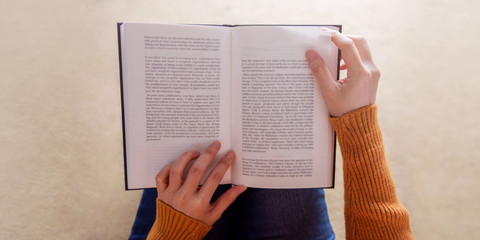 Fototapeta premium Reading Concept. Soft Focus of Young Woman Relaxing by Book in Cozy House, Sit on the Floor, Top View