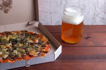 Beer and pizza. Italian pizza in a cardboard box. Light unfiltered beer on a wooden background. Favorite food set for men