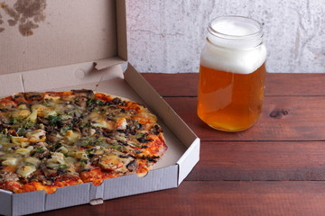 Beer and pizza. Italian pizza in a cardboard box. Light unfiltered beer on a wooden background. Favorite food set for men