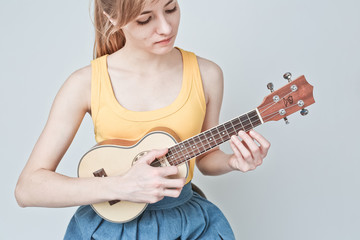 Fototapeta premium Attractive woman with light hair plays ukulele on white background