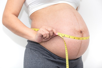 Close up of Healthy pregnancy woman measuring her belly on a white background,Image of prenatal care, maternity, health, gynecology, medicine.