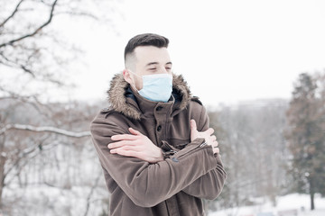 Fototapeta na wymiar Young man wearing face mask, protection from virus infection in winter time, feeling bad and cold