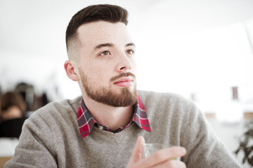 Young handsome hipster man with cup of mint tea sitting in the room in cafe