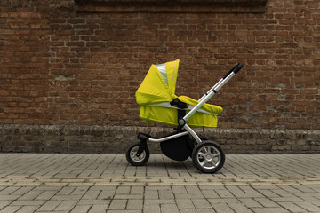 a yellow baby stroller stands on the road beside the wall