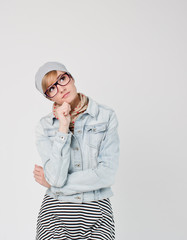 Beautiful young blond hair woman in glasses and hat  holding hand on chin and looking away. Hipster young and beautiful