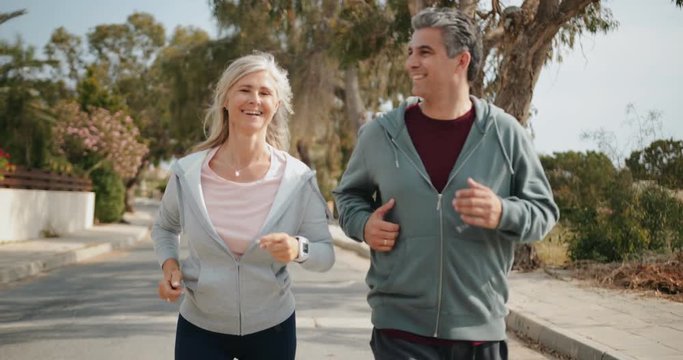 Happy mature couple jogging together on sunny day in spring
