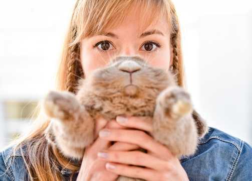 Young woman hugs big cute rabbit friend pet in her hands. Funny portrait with bunny