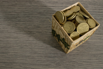 Box full of shiny euro coins on a decorated wood table