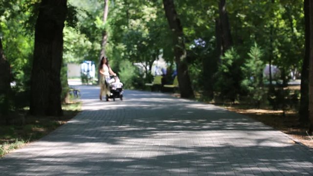 Beautiful young woman walking with baby carriage at summer park Image is blurry Slow motion
