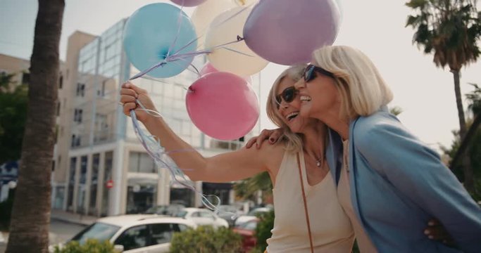Cheerful mature women celebrating with balloons in the city