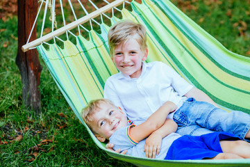 Two happy blond scandinavian excited children swinging and hugging in garden hammock together.