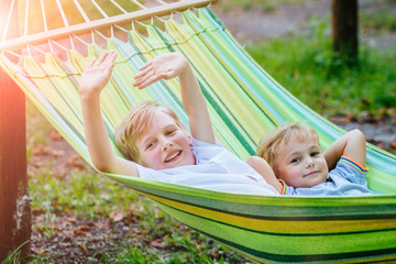 Two happy blond scandinavian excited children swinging and hugging in garden hammock together.