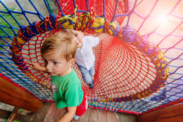 Two blond scandinavian children siblings having fun in red net tunnel in playground or amusement park. Holiday friendship and happy childhood concept.