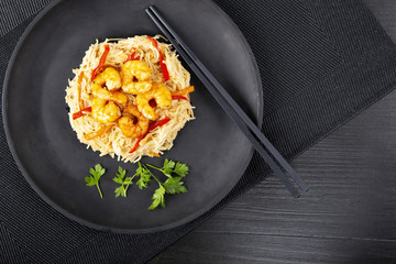 Fried prawns and rice noodles with spices on a black plate. The background is black. Top view. Eastern food. Copy space.