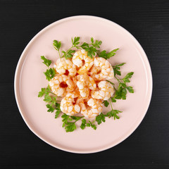 Boiled shrimp and parsley on a pink plate. Macro. The concept of healthy eating. The background is black. Copy space. A square shot. Top view.