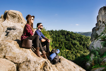 Naklejka premium A hipster traveler couple sitting together on the rocks at the mountains
