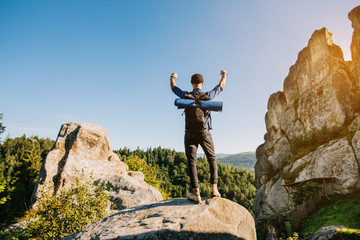 A traveler man standing on the top of the rocky mountain and holding his hands up. A cuccess concept