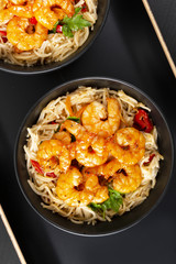 Fried prawns and rice noodles with spices on a black plate. The background is black. Top view. Eastern food.