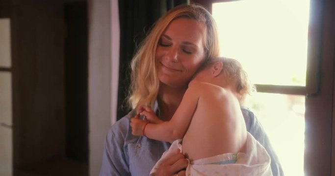 Smiling mother holding little cute grumpy baby at home